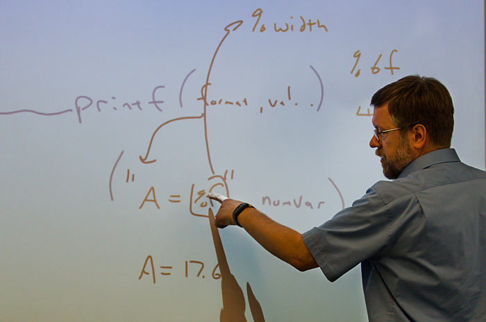 Computer Information Systems professor Alan Collard demonstrates some code on a white board.